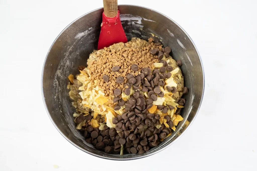 Adding potato chips, BBQ chips, Skor bits, chocolate chips, and mini marshmallows to kitchen sink cookie dough.