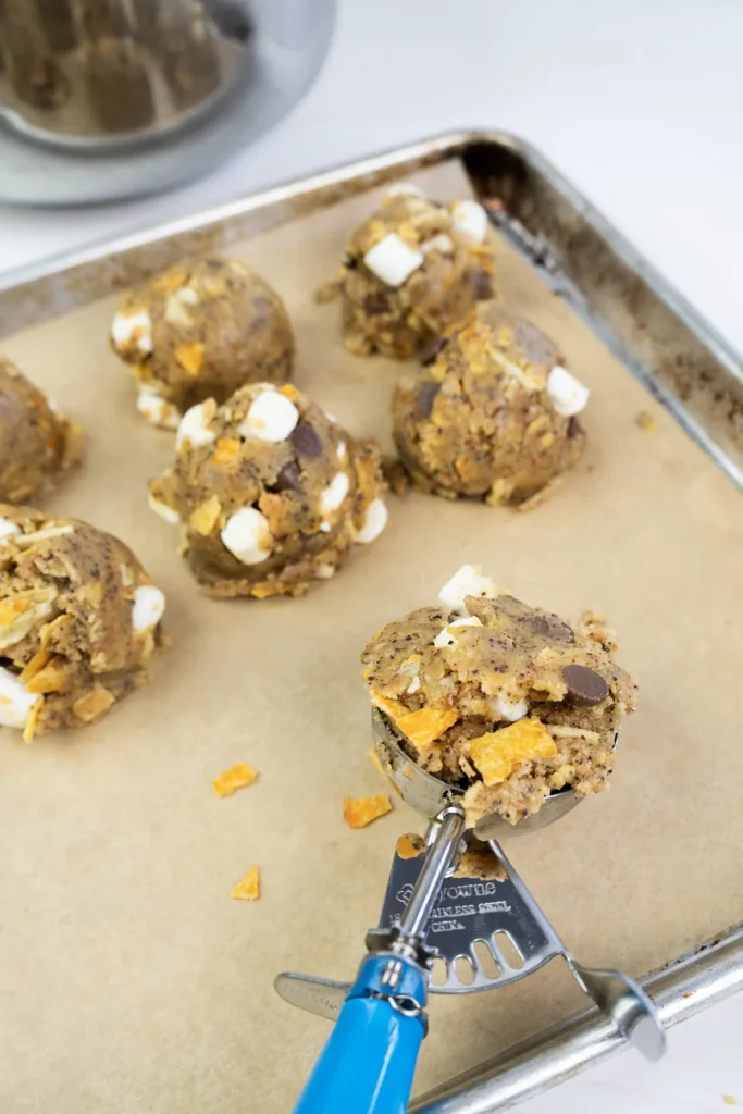 Balls of raw kitchen sink cookie dough on a baking sheet, and a cookie scoop.