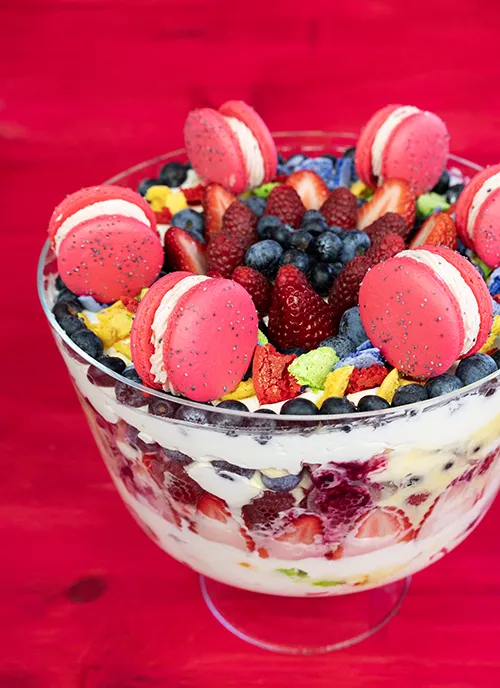 Fresh fruit trifle with macaron crumbles, fresh berries, lemon curd, and whipped cream, topped with sandwiched macarons.