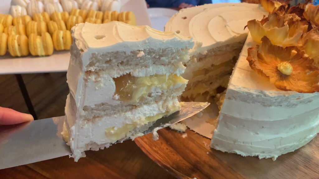 A slice of Piña Colada Dacquoise Layer Cake balancing on a knife, ready to be served.