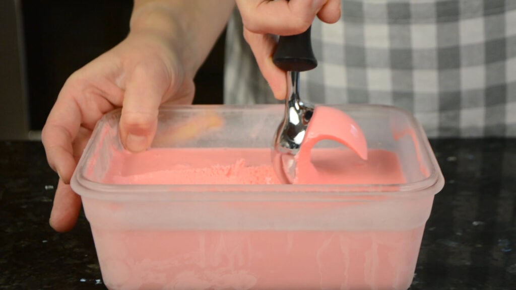 Scooping cinnamon hearts ice cream out of a container.
