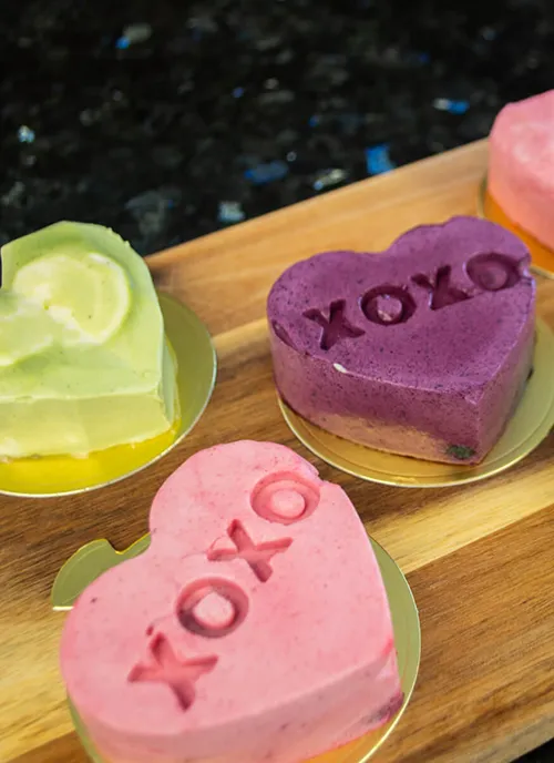 A selection of mini heart-shaped mousse cakes in matcha, blueberry, and raspberry flavours.