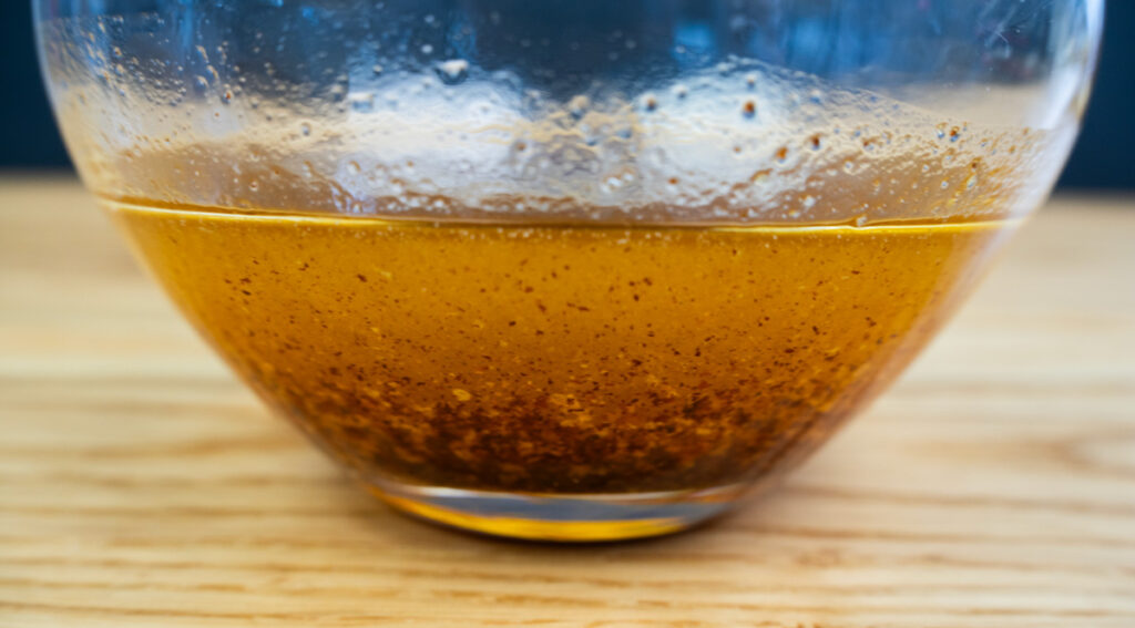 A glass of browned butter, with toasted specks of milk solids.