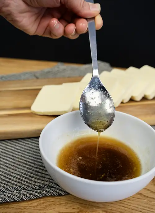 A spoon dripping brown butter into a bowl. Slices of butter on a wooden board in the background.