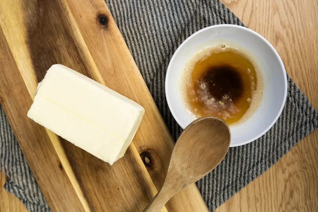 A bowl of browned butter with a wooden spoon and a brick of unsalted butter on a wooden board.