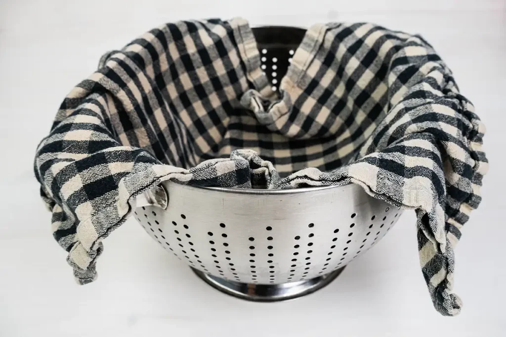 A large metal colander lined with a tea towel.