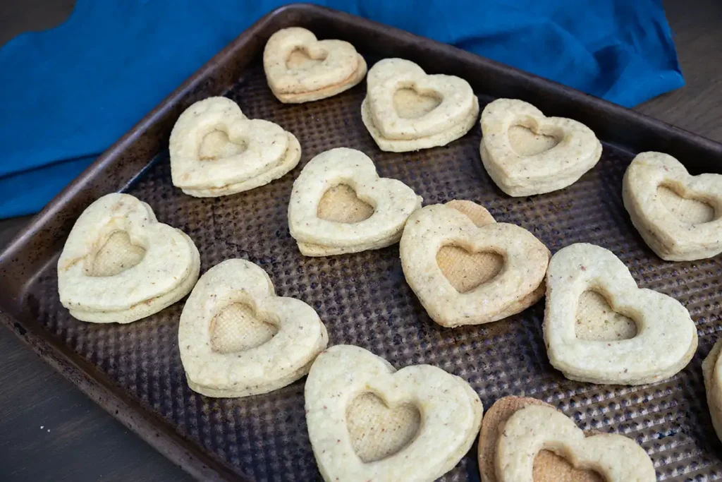 Pairs of heart-shaped cut-out sourdough cookies on a baking sheet, waiting to be filled with jam.