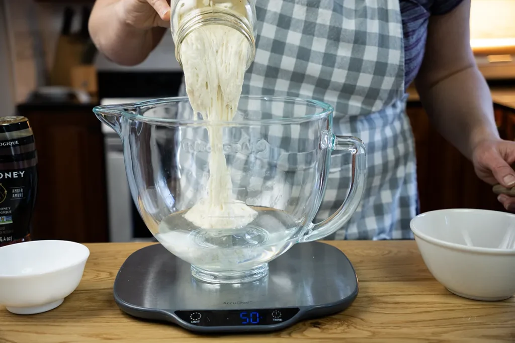 Pouring sourdough starter in a glass stand mixer bowl.