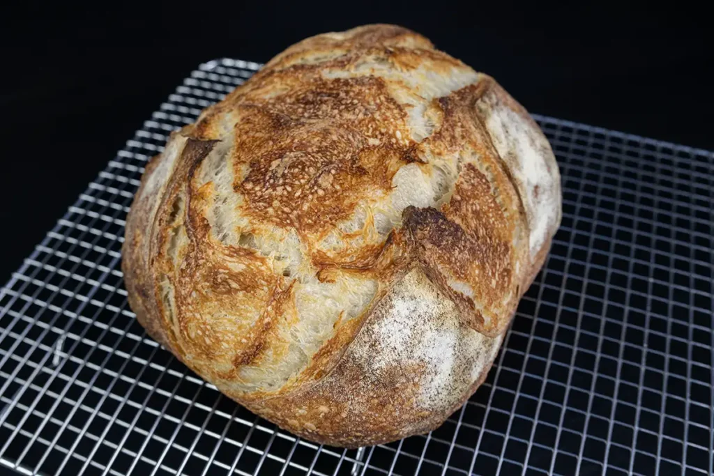 Loaf of sourdough bread on a wire cooling rack.
