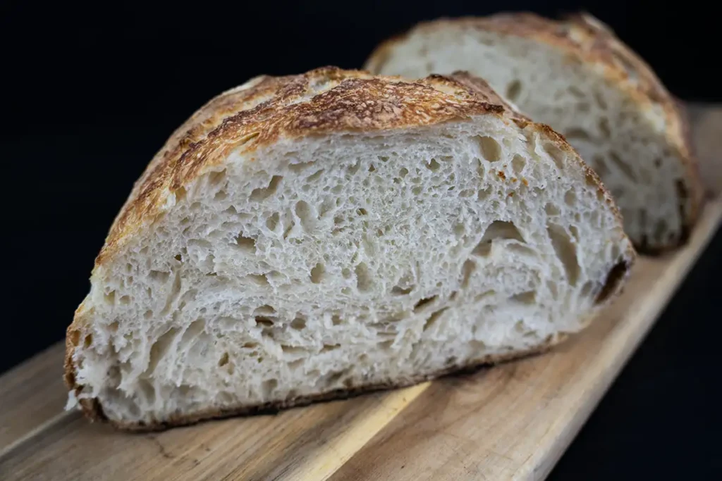 A loaf of sourdough bread sliced in half to reveal the crumb, and arranged on a wooden board.