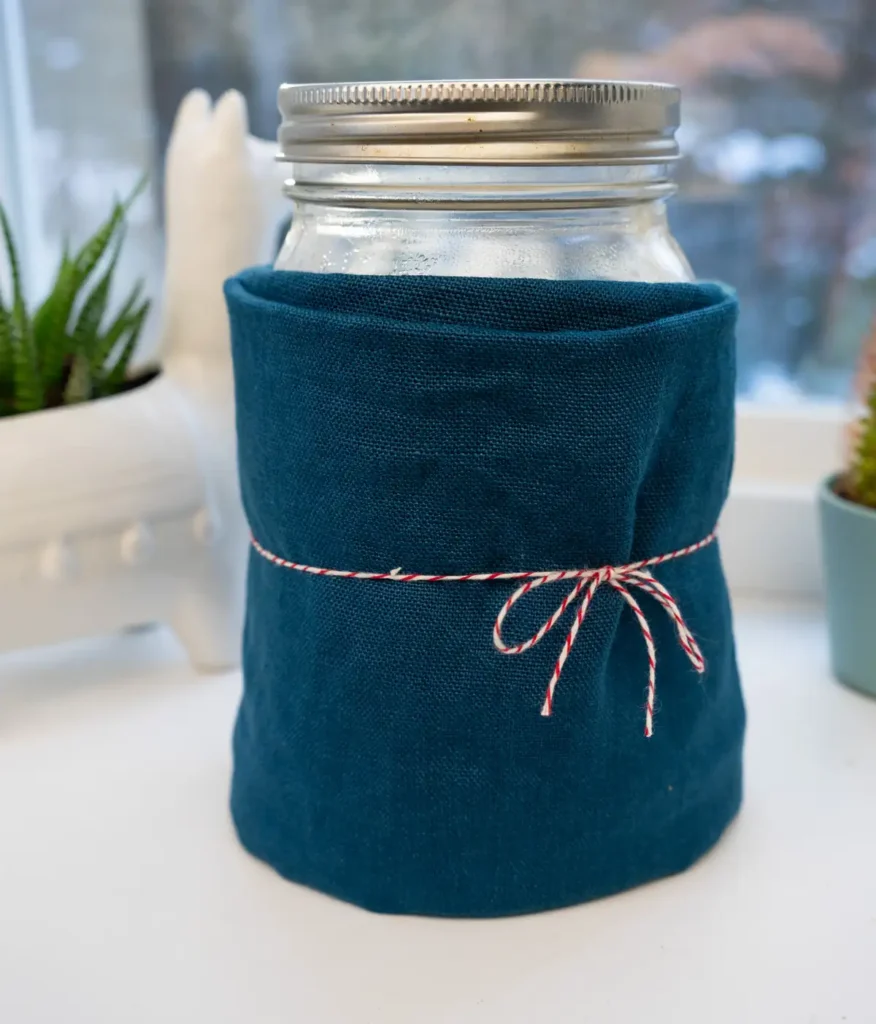 A jar of sourdough starter wrapped in fabric, on a windowsill.