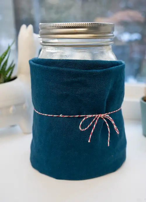 A jar of sourdough starter wrapped in fabric, on a windowsill.