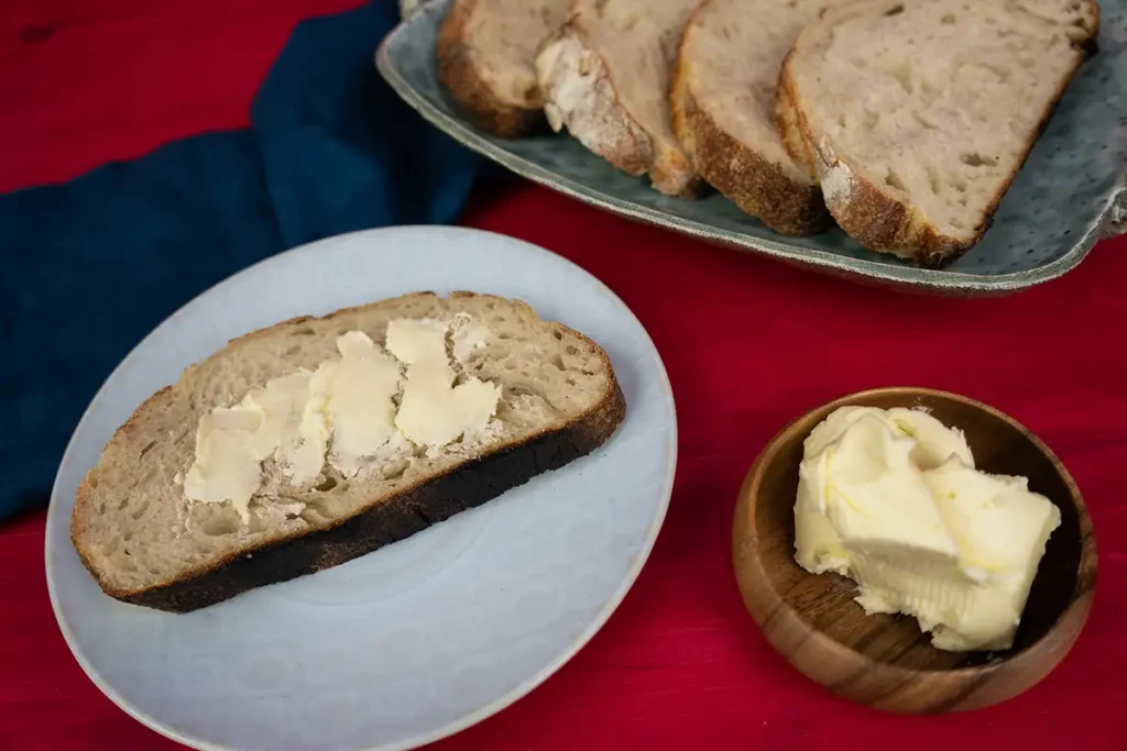 Slices of bread on a ceramic plate. One slice is on a plate, with butter.