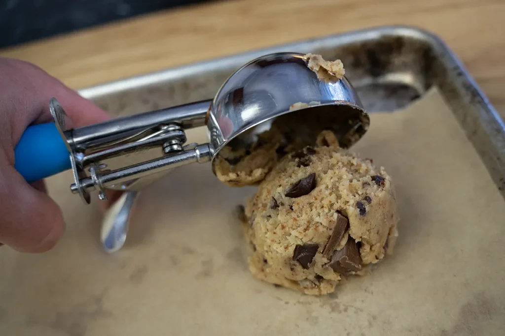 Scooping sourdough chocolate chip cookie dough onto a baking sheet lined with parchment paper.