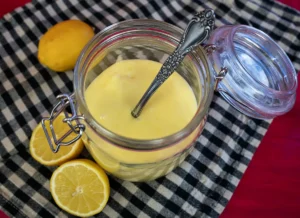 Jar of lemon curd with fresh lemons in the background.