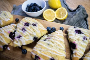 Sourdough discard blueberry scones on a wooden board, with a couple fresh lemons and a bowl of fresh blueberries in the background.