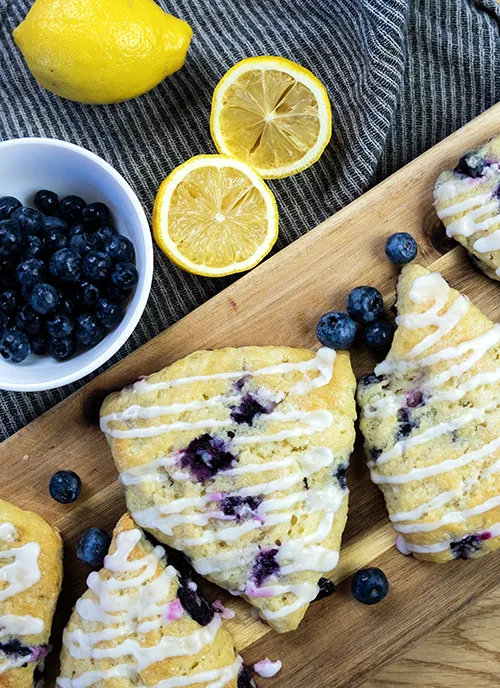 Sourdough blueberry scones arranged on a wooden board with fresh blueberries, along with lemons and a bowl of blueberries.