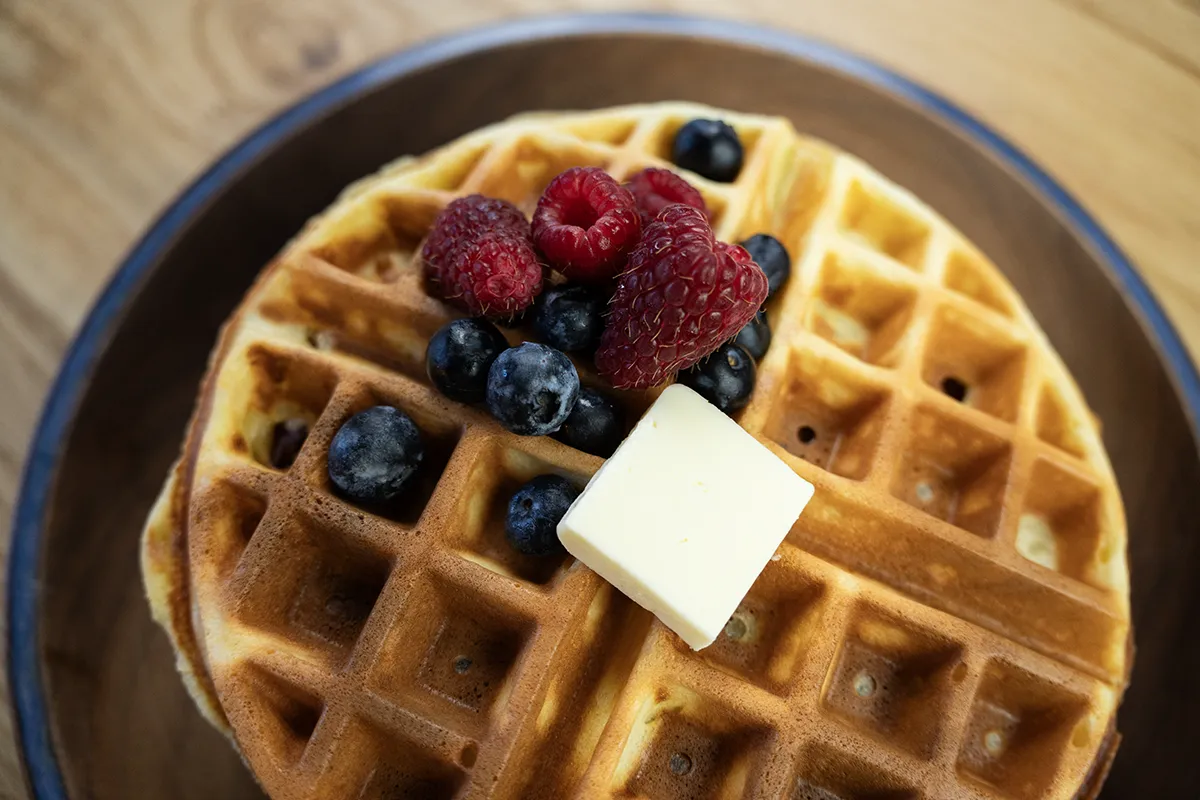 Sourdough waffle on a wooden plate, topped with butter, maple syrup, and fresh berries.