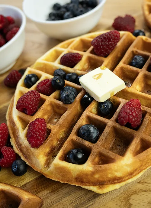 Sourdough waffle topped with a square of butter, maple syrup, and fresh berries.