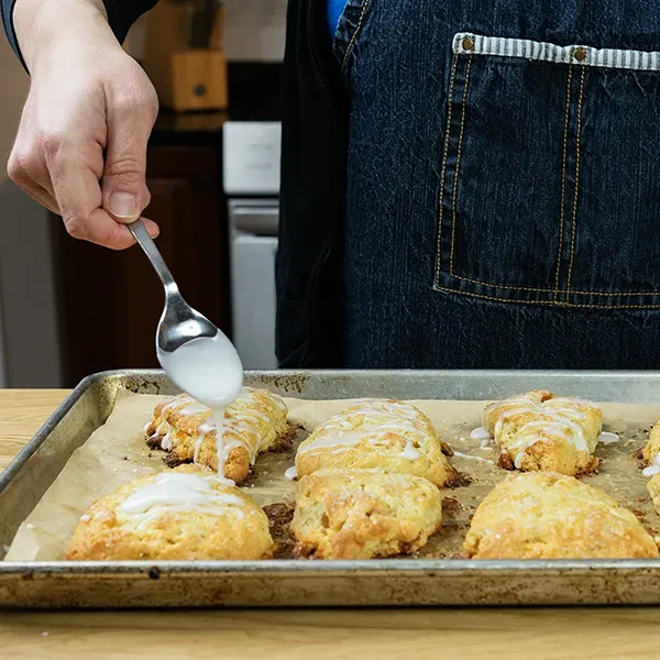 Drizzling powered sugar glaze over scones.