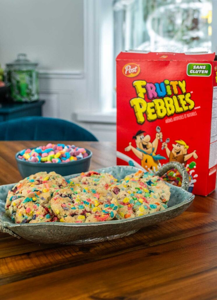 Tray of Lucky Charms Cookies with Fruity Pebbles, with a bowl of Lucky Charms marshmallows and a Fruity Pebbles box in the background.