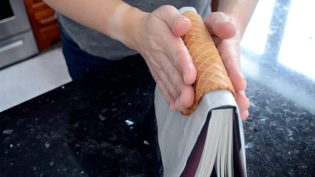 Shaping a hot waffle cone fresh out of the waffle cone maker, over a book to make it into taco shell.