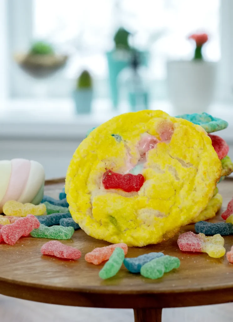 A Sour Patch Kids cookie on a pile of Sour Patch Kids candies on a wooden cake plate.