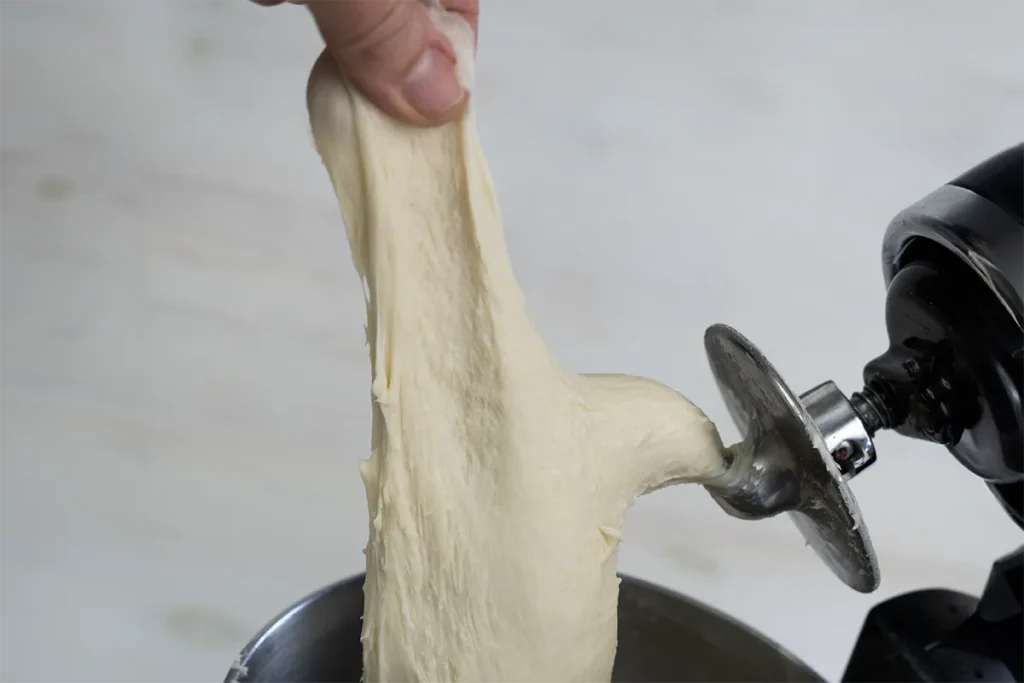 Pulling a piece of dough from a dough hook to check if enough gluten has been developed.