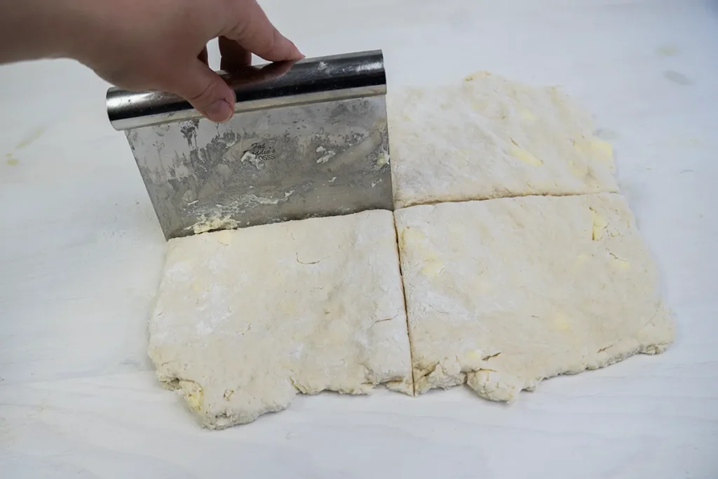 Cutting sourdough biscuit dough into quarters for layering.
