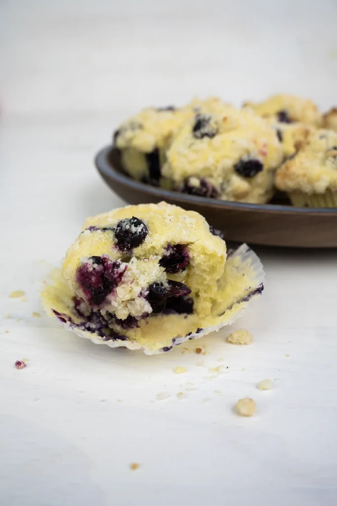 Plate of baked sourdough blueberry lemon muffins. In the foreground is one muffin with a bite taken out of it.