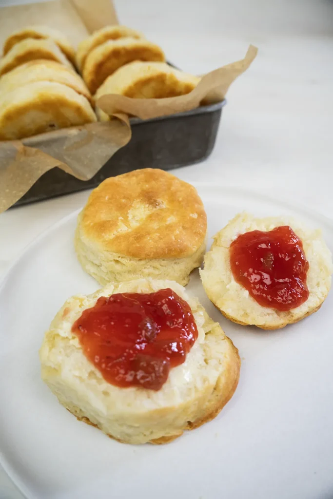 A plate with a cut open sourdough biscuit spread with strawberry jam.