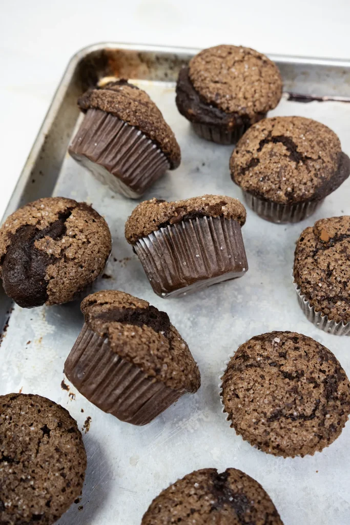 Sourdough discard double chocolate banana muffins scattered on a baking sheet.