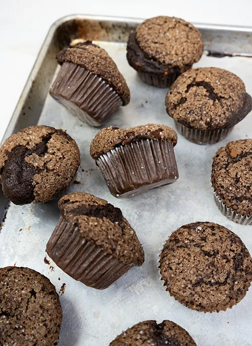 Sourdough double chocolate banana muffins scattered on a baking sheet.