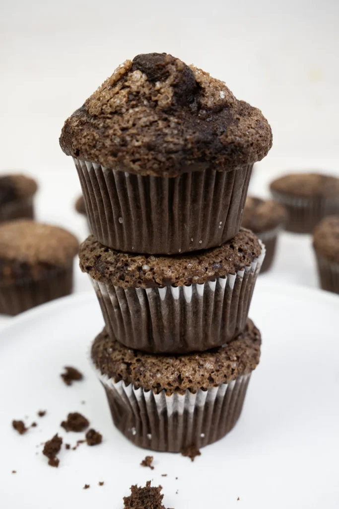 Stack of 3 baked sourdough double chocolate banana muffins in white paper wrappers.