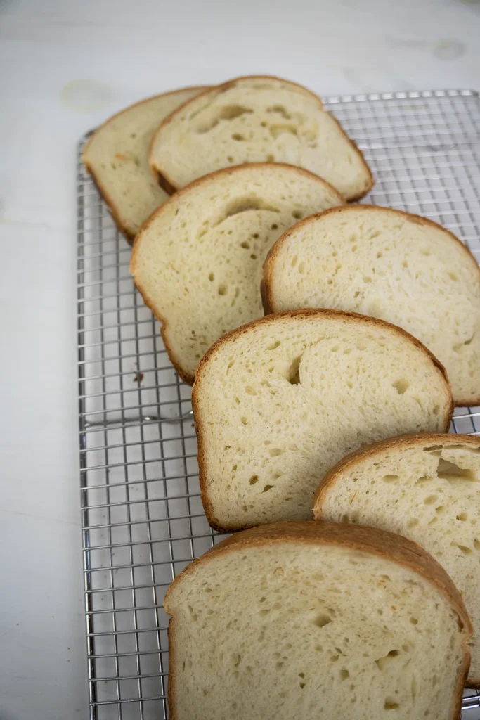 Slices of sourdough sandwich bread arranged on a wire cooling rack.