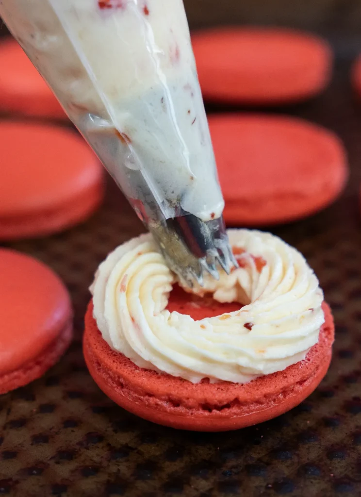 Piping a ring of buttercream on a macaron shell.
