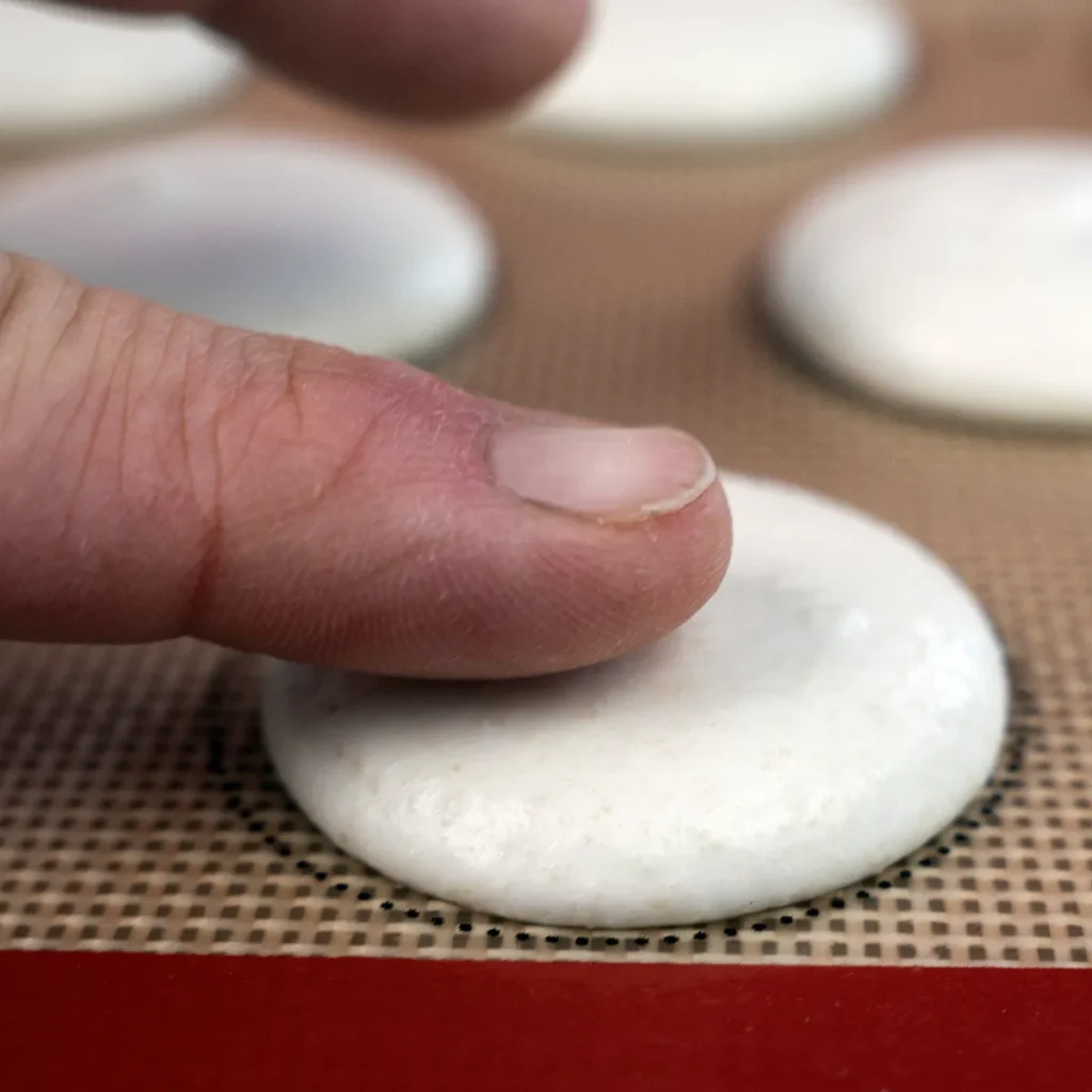 Touching a macaron to test if it has dried enough.