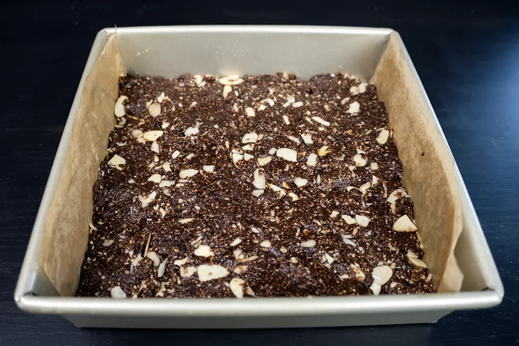 The bottom (chocolate-graham-coconut) layer of a Nanaimo bar, pressed into a square pan.