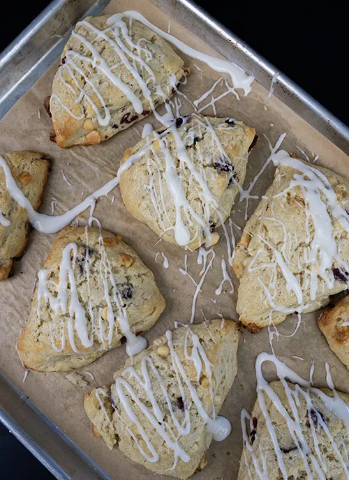 Top-down view of glazed sourdough discard scones with cranberry and white chocolate, arranged on a baking sheet.
