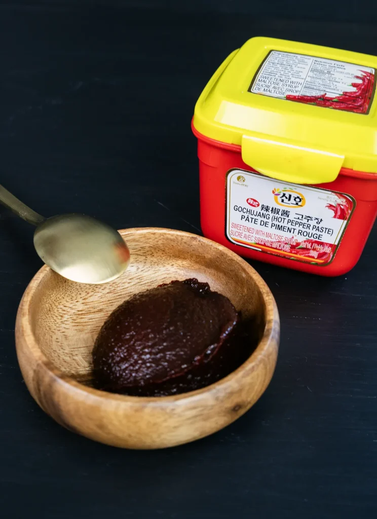 A package of gochujang, and a little wooden bowl filled with gochujang.