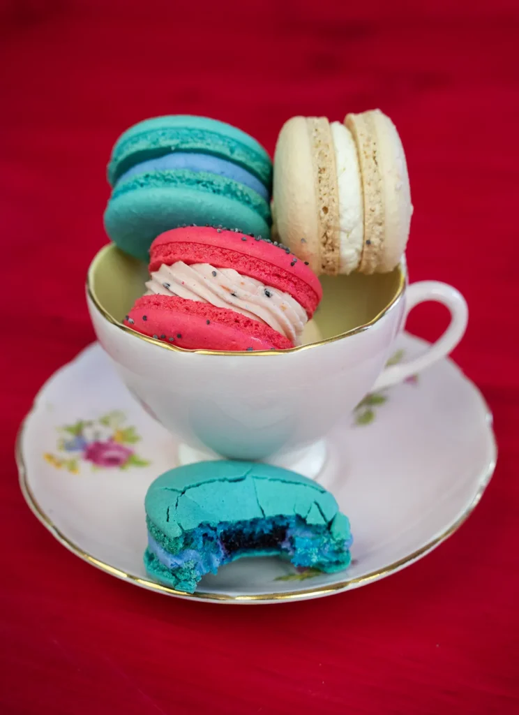 Colourful macarons in a teacup. One macaron with a bite is in the foreground.