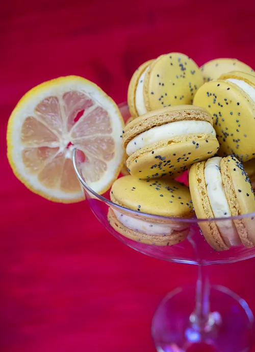 Lemon poppyseed macarons piled in a stemmed glass garnished with a lemon slice.