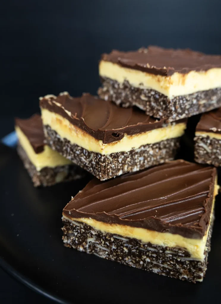 Nanaimo bars arranged in a pile on a plate.