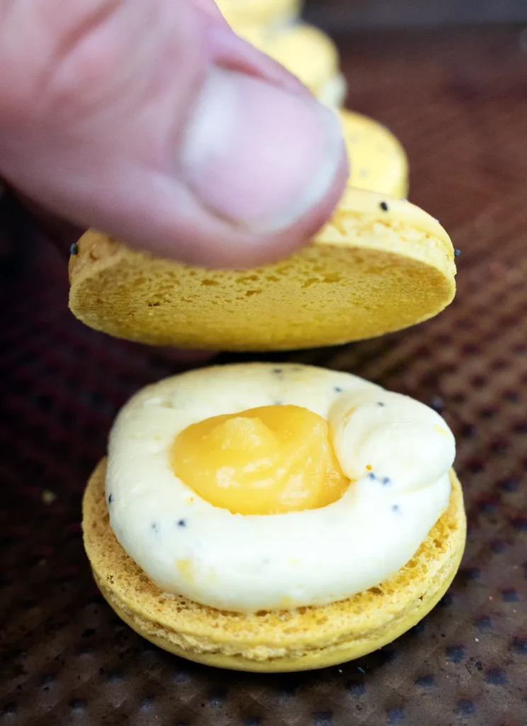 Placing a matching macaron shell on top of the filling.
