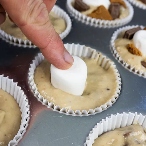 Pressing a frozen marshmallow into the center of a muffin cup filled with sourdough banana s'mores batter.
