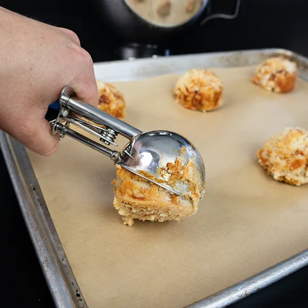 Scooping sourdough gochujang caramel cookie dough onto a parchment-lined baking sheet.