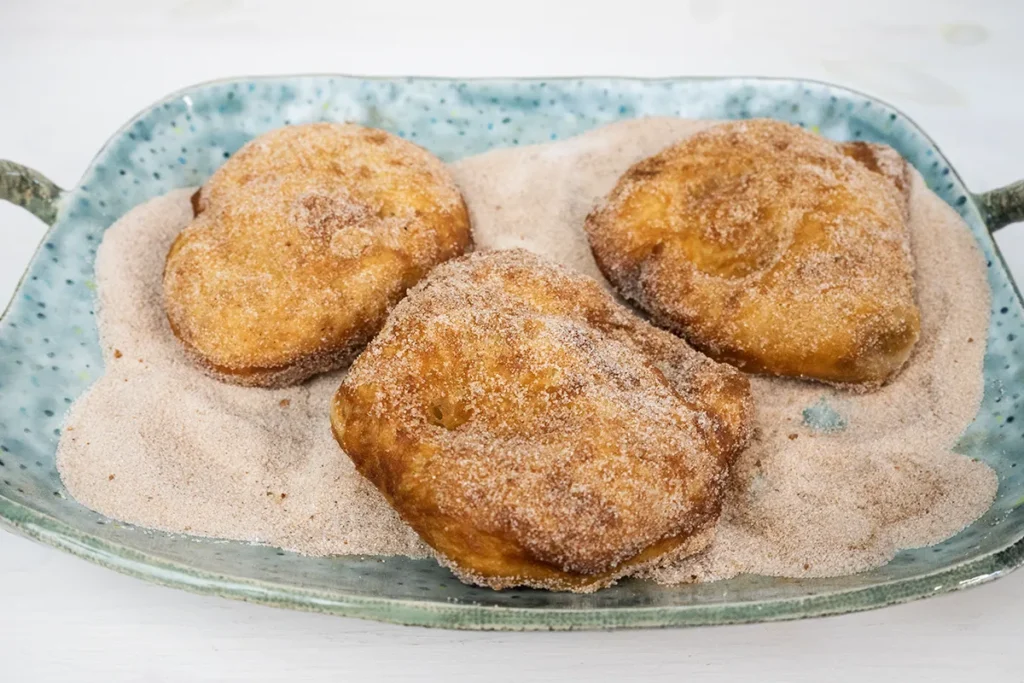 Coating mini sourdough Beaver Tails in cinnamon sugar.