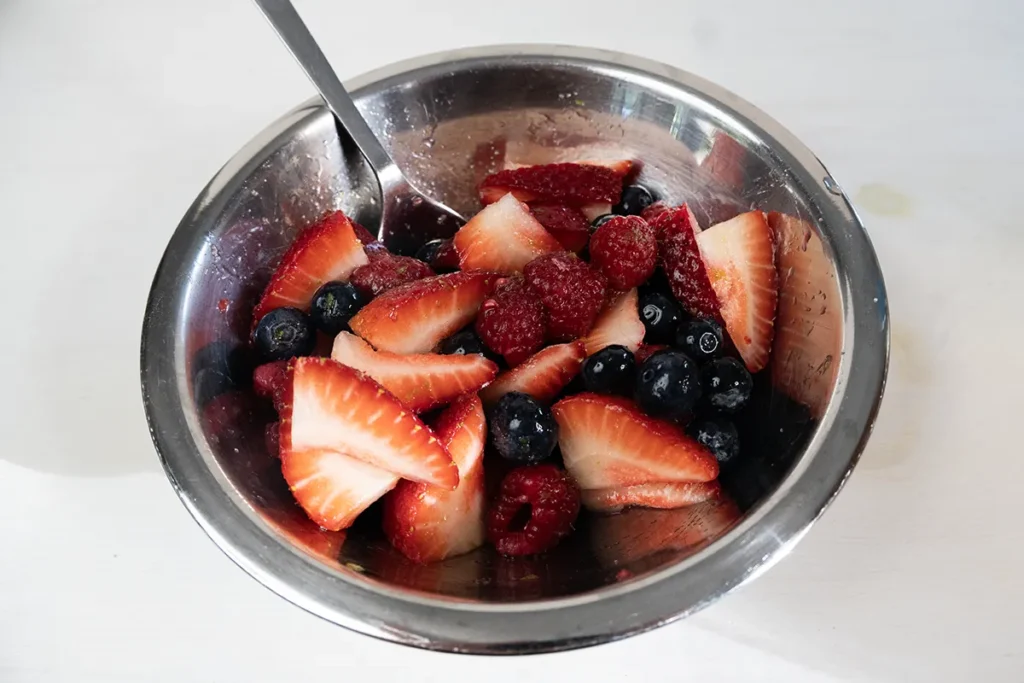 Macerating fresh berries with sugar, citrus zest, and citrus juice.