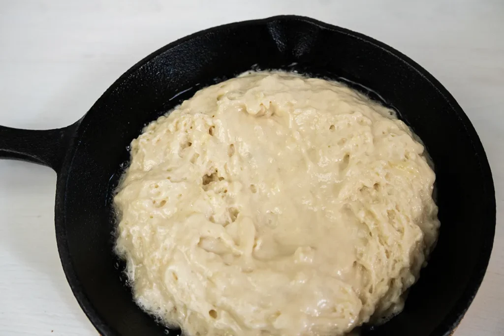 Filling a skillet halfway with pancake batter.