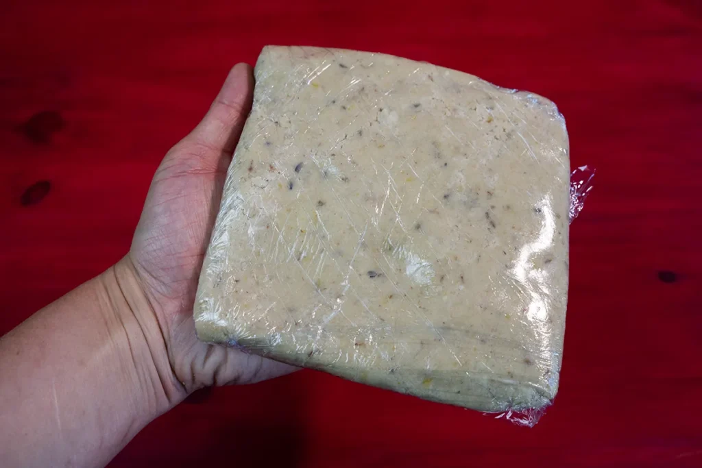 A square of lemon lavender shortbread cookie dough wrapped in plastic wrap, ready to be chilled.